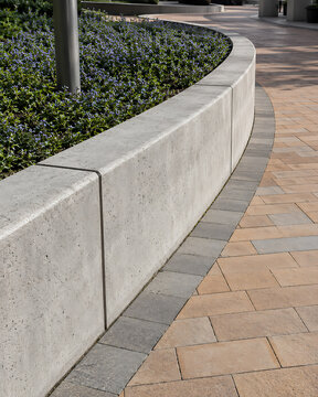 Curved concrete edging defines a walkway alongside a flowerbed in a garden setting