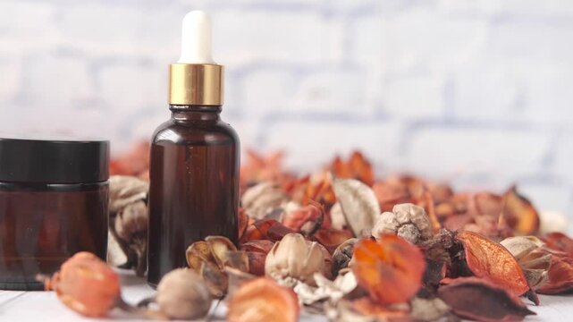 A captivating close-up of amber glass dropper bottles and cream jars, surrounded by dried potpourri, creating a soothing and natural beauty product display in soft motion footage