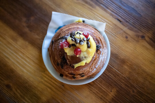 Brioche sfogliata gourmet con gocce di cioccolato guarnita con crema pasticcera e frutti di bosco freschi su un tavolo di legno rustico