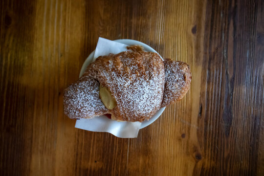 Croissant fragrante farcito con crema pasticcera e spolverato con zucchero a velo servito su un piattino sopra un tavolo in legno