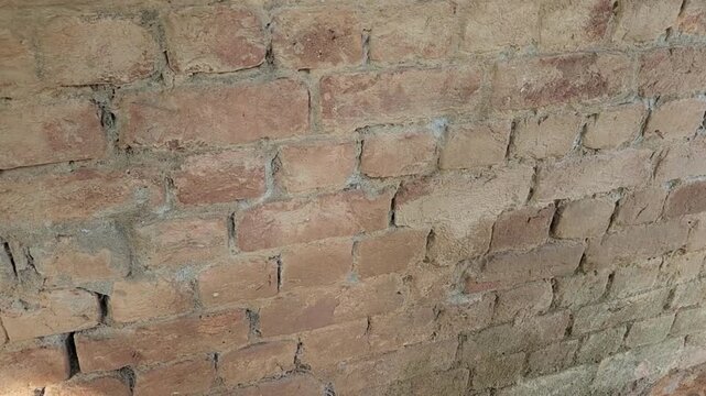 Brick wall built with aged red clay blocks showing weathered mortar joints and uneven rustic surfaces, capturing the historic masonry texture and construction detail in daylight conditions.