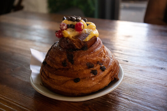 Brioche sfogliata gourmet con gocce di cioccolato guarnita con crema pasticcera e frutti di bosco freschi su un tavolo di legno rustico
