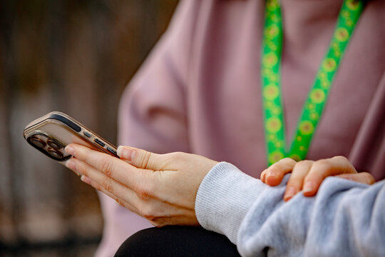 Close-up of womans hand holding a smartphone while sitting on an urban bench