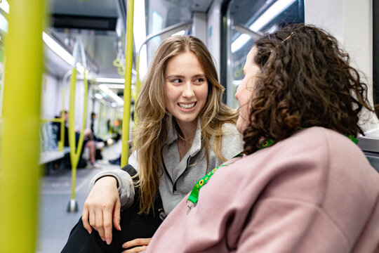Two young women seated on a patterned seat inside the train