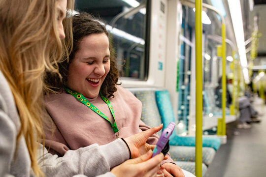 Young woman sitting beside a teenage girl with curly hair holding a tablet on a patterned train seat