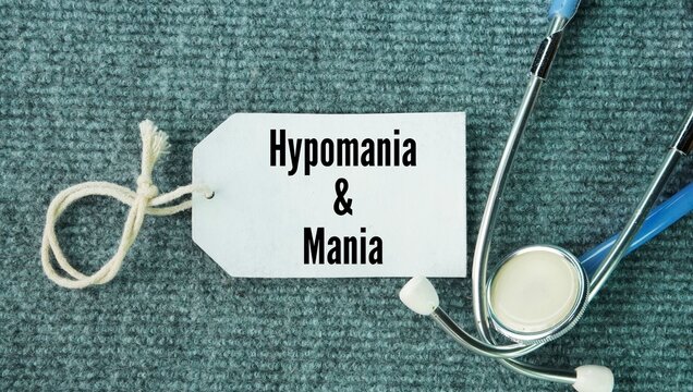 Stethoscope and paper tags with the words Hypomania and mania. periods of excessively high energy, activity, and an elevated or irritable mood