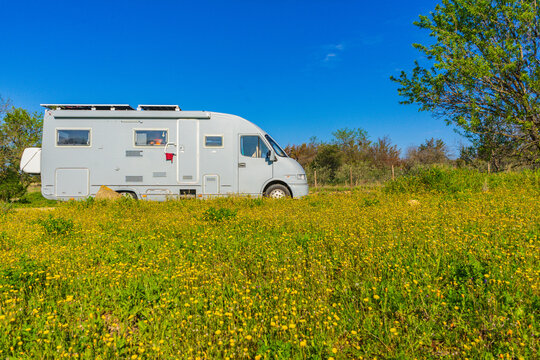 Camping car rv parked close to spring meadow with yellow flowers with blue sky during daytime