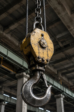 Industrial lifting hook hangs from a steel cable and chain in a warehouse