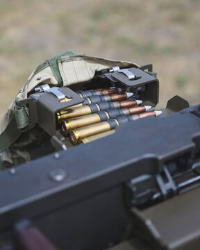 Close up view of linked ammunition cartridges arranged in a metal ammunition box beside a heavy machine gun. 