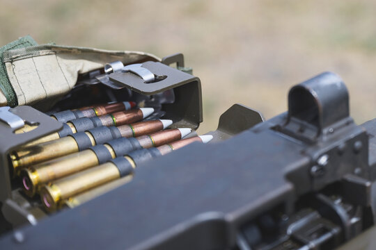 Close up view of linked ammunition cartridges arranged in a metal ammunition box beside a heavy machine gun. 