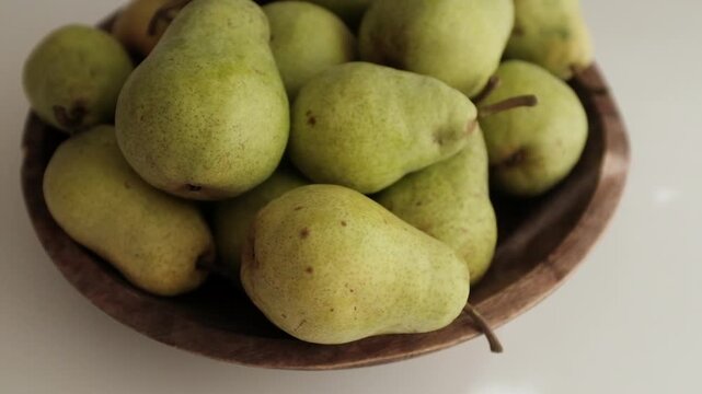 Fresh green pears piled inside a dark rustic wooden bowl on a clean white surface. Ideal for culinary commercials, healthy eating campaigns, nutrition blogs, organic farm promotions, and cooking tuts
