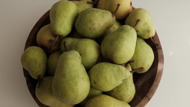 Fresh green pears piled inside a dark rustic wooden bowl on a clean white surface. Ideal for culinary commercials, healthy eating campaigns, nutrition blogs, organic farm promotions, and cooking tuts