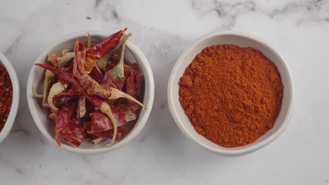Close up overhead shot of three bowls with dried chili peppers and chili powder.