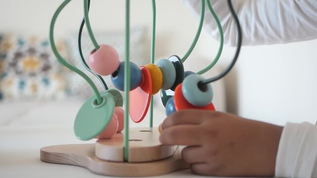 Close up video of little child hands playing with a wooden bead maze toy with colorful beads on a white background