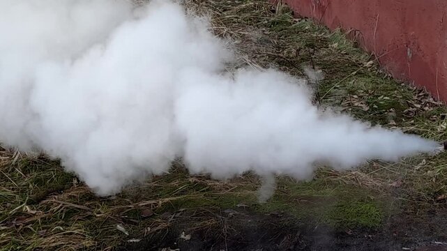 Heavy white smoke and steam escaping from a basement drainage pipe of an old brick public building with windows, depicting a city infrastructure utility failure and emergency accident.