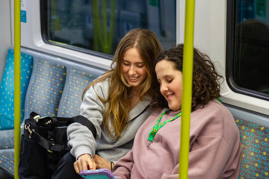 Two young women sitting side by side on a patterned seat inside a train carriage