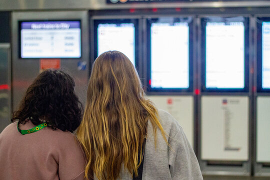 Back profile of two young women standing facing a row of digital information screens