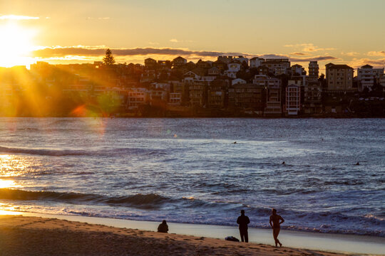 Beachgoers relaxing beside ocean waves at golden sunset with surfers in the water