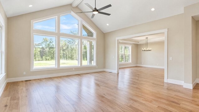 Spacious modern living room interior, vaulted ceiling with large windows, light hardwood floors, neutral beige walls, empty new home design for real estate marketing