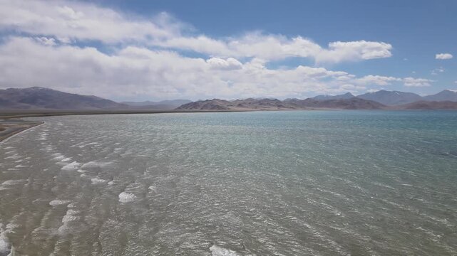 Aerial drone view of Karakul Lake in the Pamirs, with waves, a barren mountain landscape and a smooth circular flight