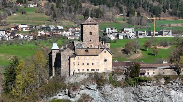 rocky outcrop cliff ortenstein castle square tower onion dome tomils village rooftops apartment buildings construction crane domleschg valley graubunden switzerland aerial drone orbit heritage site