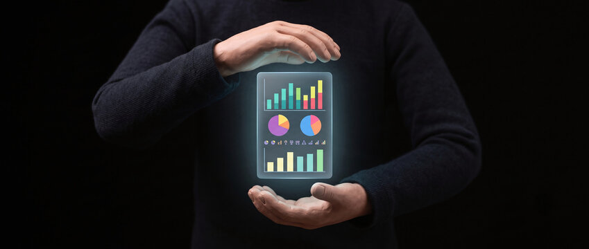 Person holding glowing digital data dashboard interface with bar charts and pie graphs on black background.