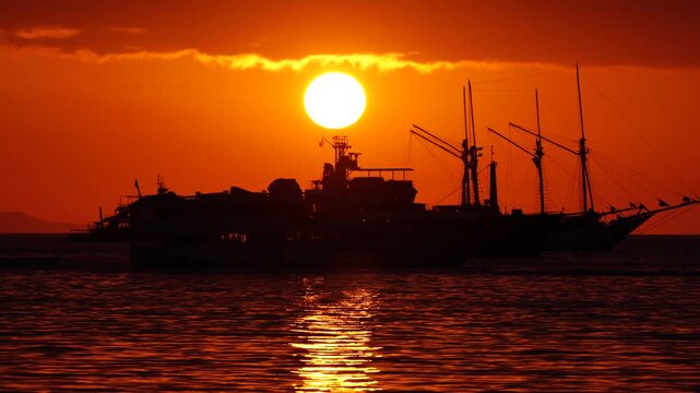 Luxury Phinisi Boat Sailing on Labuan Bajo Ocean at Sunset, Tropical Landscape View with Golden Orange Sky and Calm Sea, Flores, East Nusa Tenggara, Indonesia