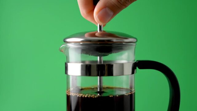 Hand pressing plunger of glass french press with coffee on green screen background