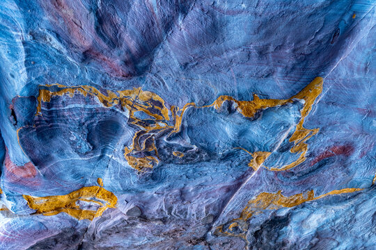 View of vibrant mineral patterns on the sandstone walls of a tomb in Petra, showcasing swirling blue, purple, and yellow ochre veins in Wadi Musa, Ma'an Governorate, Jordan.