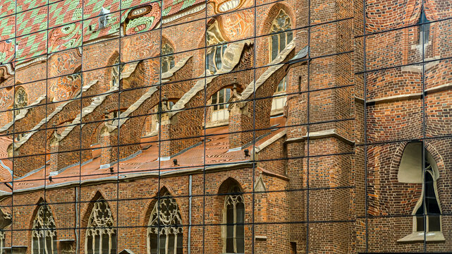 Abstract reflection of a historic Gothic brick church on a modern glass facade.