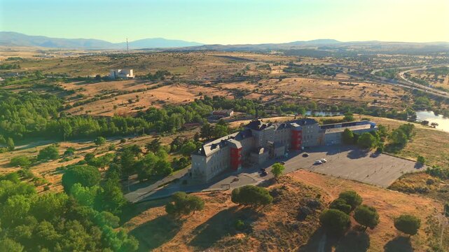 An isolated modern building near Avila, Spain, stands amid dry grassland with mountains in the distance.