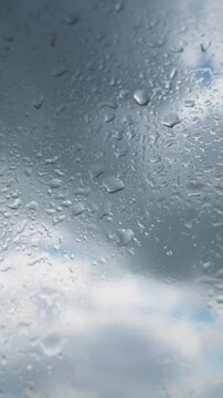 Water droplets condense and slide down clear glass against an overcast sky. Natural ambient daylight illuminates soft organic shapes across the smooth surface during daytime.