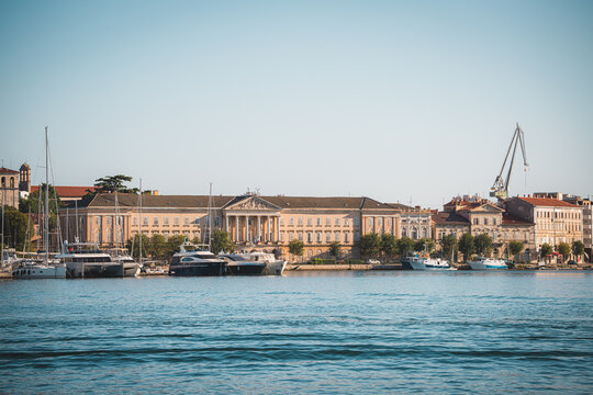 View of the historic waterfront in Pula featuring neoclassical architecture, moored yachts, and a harbor crane in Pula, Istria County, Croatia.