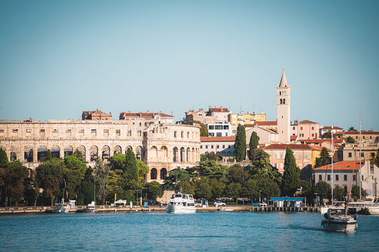 View of the historic Pula Arena amphitheater overlooking the waterfront with boats and traditional architecture in Pula, Istria County, Croatia.