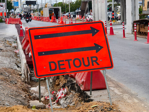 Orange detour sign with black arrows beside closed road construction site and street cones