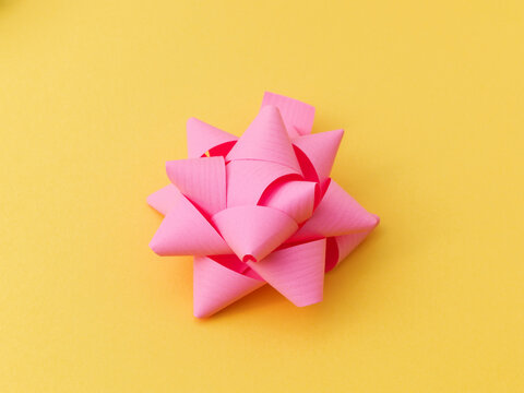 Single Pink Gift Ribbon Bow on Yellow Background