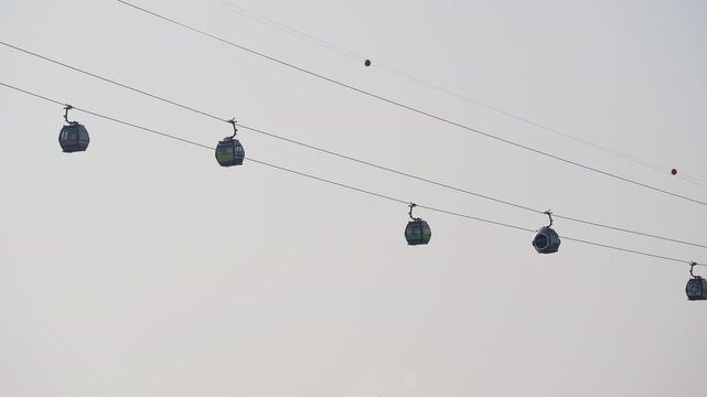 Cable car cabins moving along overhead wires against an open pale sky.
