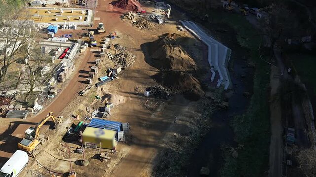 Aerial top-down view of an active urban construction site with excavators and machinery beside a narrow river