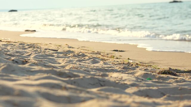 Gentle sea waves rolling onto a golden sandy beach in a low angle coastal landscape shot