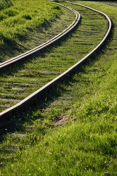 Curving railway tracks overgrown with green grass on a sunny day