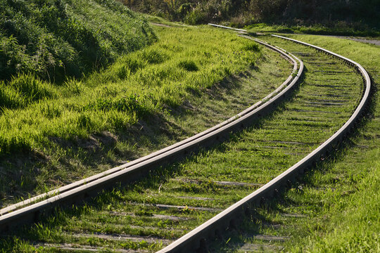 Curved railway track running through green grassy terrain in sunny countryside