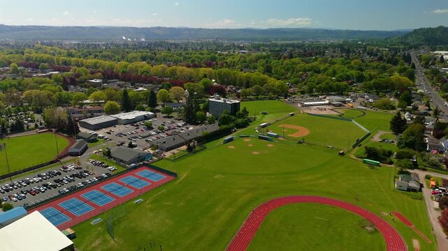 Aerial flight above a school sports complex with tennis courts track and baseball fields
