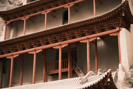 View of the historic Mogao Caves featuring traditional red wooden architecture with intricate bracket systems set against a stone cliff in Jiuquan, Gansu, China.