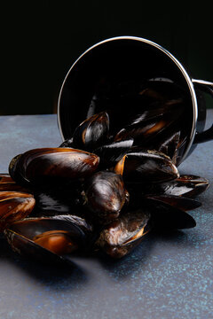 Black mussels spilling from metal pot on blue textured surface food