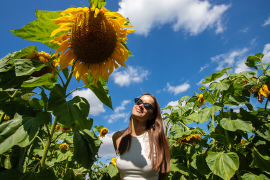 confident young woman poses among giant sunflowers under a vivid blue sky, representing freedom, self acceptance, joyful femininity, summer wellbeing and personal growth