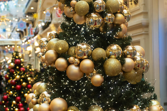 decorated christmas tree with shiny and matte gold baubles, glitter spheres and twinkling lights, festive installation inside a shopping arcade with blurred holiday decorations
