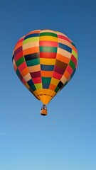 Obraz premium Vibrant Colorful Hot Air Balloon Flying High in Clear Blue Sky Skyward View of Patterned Aerostat Envelope and Passenger Wicker Basket for Adventure Travel Aviation and Freedom Concept Background