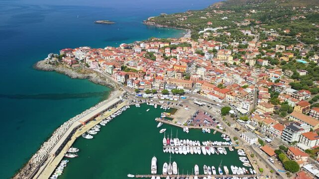 Marina di Camerota aerial drone flyover of scenic authentic town peninsula with white boats in harbor. Orange tile roofs and rugged coves in Cilento Italy 4K