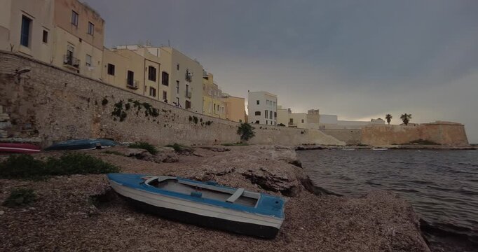 Wooden Fishing Boat on Rocky Beach with Bastione Conca in the Distance, Trapani, Italy