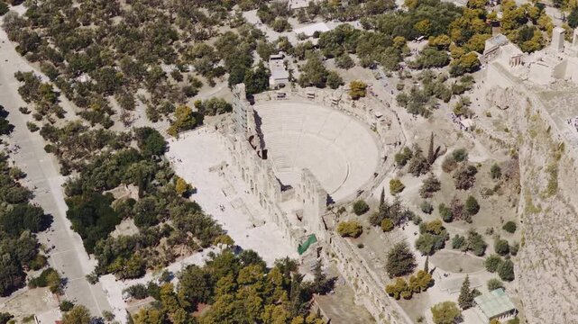 High aerial perspective showing the ancient Odeon of Herodes Atticus, a historic roman stone theatre on the slope of the Acropolis of Athens, with tourists exploring the famous landmark